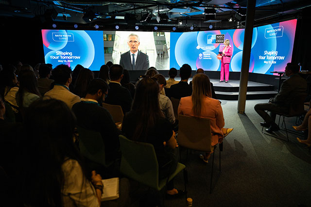 Publiken fotograferad bakifrån medan de lyssnar på Jens Stoltenberg på skärm